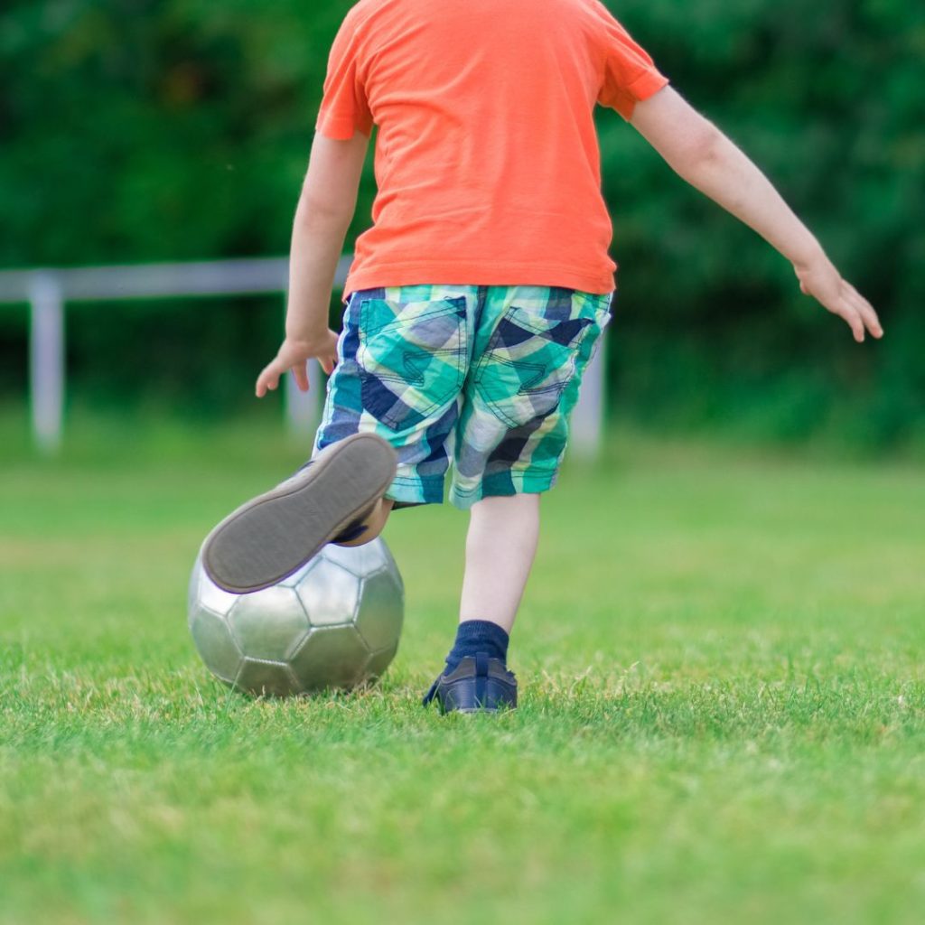 Young child kicks a silver soccer ball on the grass